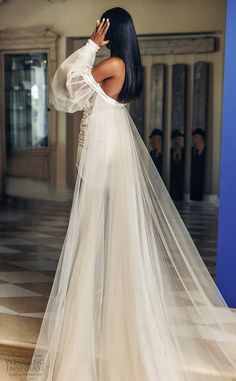 the back of a woman wearing a white wedding dress with long veil on her head