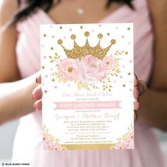 a woman holding up a pink and gold baby shower party card with flowers on it