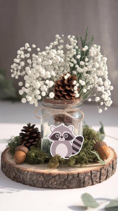 a glass jar filled with white flowers and a raccoon sticker sitting on top of a tree stump