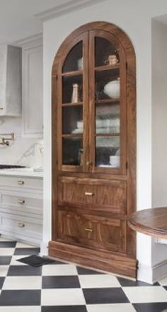 a kitchen with black and white checkered flooring, wooden cabinets and an arched glass door