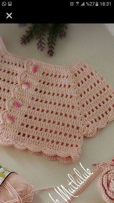 a crocheted pink sweater and hat on a table with knitting needles next to it