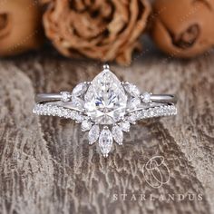 an engagement ring with a pear shaped diamond surrounded by smaller pears on a wooden surface