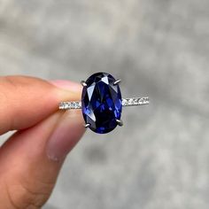 a woman's hand holding an oval shaped blue sapphire and diamond ring with white diamonds