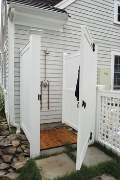 an open white door on the side of a house next to a stone walkway and fence