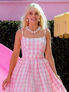 a woman in a pink and white checkered dress smiles as she stands next to a pink slide
