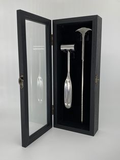 an open black box with a silver spoon and tongs in it on a white surface