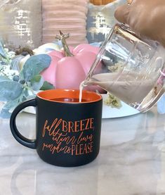 someone pours milk into a coffee mug on a table with pink and white pumpkins