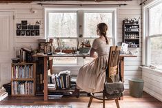 a woman sitting at a desk in front of a window with lots of books on it