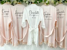 three pink robes hanging up against a wall with white flowers and greenery in the background