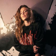 a beautiful young woman sitting on top of a skateboard next to a graffiti covered wall