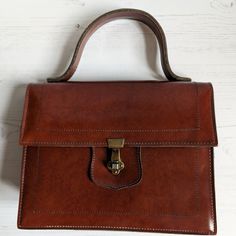 A lovely vintage brown handbag with a carry handle and in a traditional boxy shape The handbag is made from brown faux leather. There in one large internal compartments with a smaller zip pocket on the inside. The handbag fastens with a metal clasp which is still very strong The handbag measures approx 22.5cm x 19cm x 6cm. The strap is 24cm long. The bag is in really good condition Ideal bag to complete a vintage outfit 60s Bags, Thrift Inspo, Vintage Leather Handbag, Style Goals, Vintage Handbag, Vintage Outfit, Top Handle Bags, Brown Handbag, Mid Century Vintage