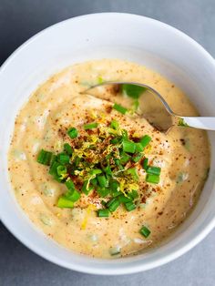 a white bowl filled with soup topped with green onions and seasoning next to a spoon