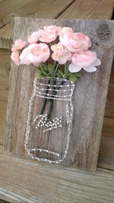 a mason jar filled with pink flowers on top of a wooden table next to a piece of wood