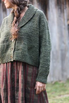 a woman standing in front of a wooden fence wearing a green sweater and striped skirt