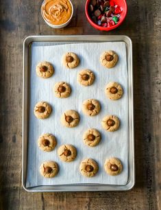 peanut butter and jelly cookies on a baking sheet with bowls of candy in the background