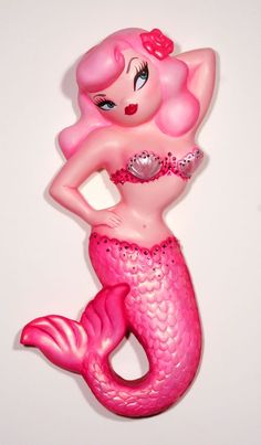 a pink mermaid figurine sitting on top of a white wall