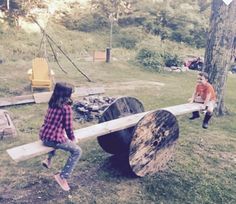 two children are playing on a log in the yard while another child watches from behind