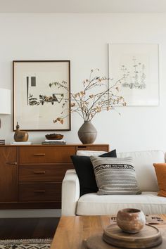 a living room with white couches and wooden tables in front of paintings on the wall