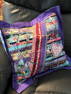 a purple patchwork pillow sitting on top of a black leather couch next to a chair