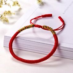 a red string bracelet sitting on top of a white book next to flowers and leaves