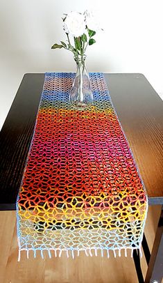 a vase with flowers sitting on top of a table next to a knitted table runner