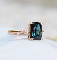 an engagement ring with a large blue stone and diamonds on the side, sitting on top of a white surface