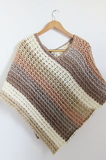 a crocheted sweater hanging on a wooden hanger next to a white wall