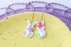 two bunny shaped earrings sitting on top of a yellow plate next to a purple basket