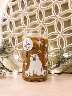 a glass jar with a bear and snowflakes on it sitting next to pine branches