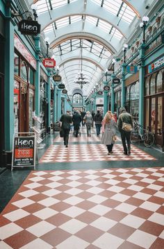 people are walking through an indoor shopping mall with checkered flooring on the ground