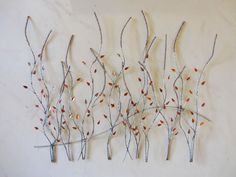 three metal branches with red and white leaves hanging on a wall in front of a white wall