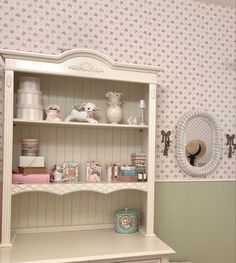 a white china cabinet sitting next to a wall covered in pink and white wallpaper