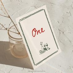 a card with the word one written on it next to a vase filled with flowers