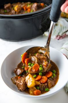 a white plate topped with meat and veggies next to a pot of stew