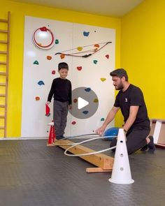 two men are playing with an obstacle course in a playroom that is painted yellow and white