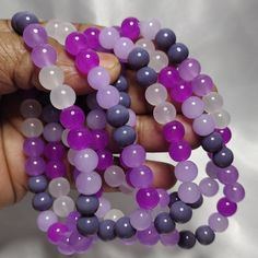 a person holding beads in their hand on a white surface with grey and purple colors