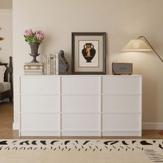 a white dresser sitting in a living room next to a lamp and pictures on the wall