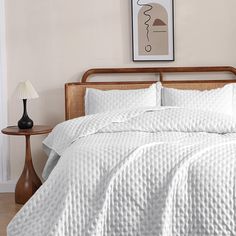 a bed with white comforter and pillows in a room next to a lamp on a table