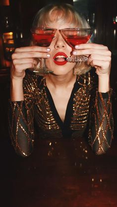 a woman with red lipstick holding up two wine glasses to her face while sitting at a table