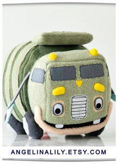 a green bus stuffed animal with yellow and black eyes, sitting on top of a white surface