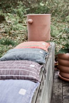 several pillows are lined up on a wooden bench in the woods, with a potted plant next to them