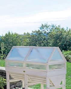 a small white greenhouse in the middle of some grass