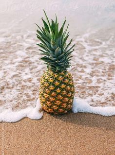 a pineapple sitting on top of a sandy beach next to the ocean with waves coming in