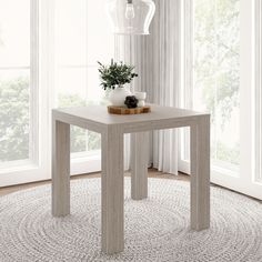 a table with a potted plant on it in front of two windows and a rug