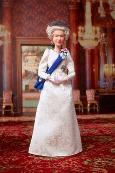 a doll in a white dress and tiara standing on a red carpeted area