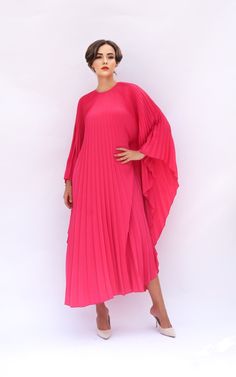 a woman wearing a pink dress with pleated sleeves and heels standing in front of a white background