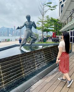 a woman standing next to a fountain with a statue in the background