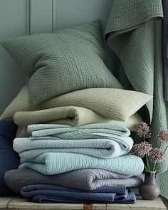 a stack of folded blankets and pillows on a table next to a vase with flowers