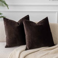 two brown pillows sitting on top of a white couch next to a potted plant