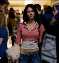 a woman in jeans and a pink shirt is walking through an airport with her hand on her hip